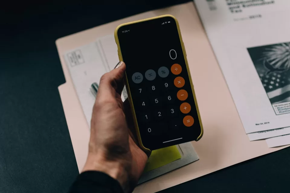 Hand holding a phone with a calculator app above printed forms