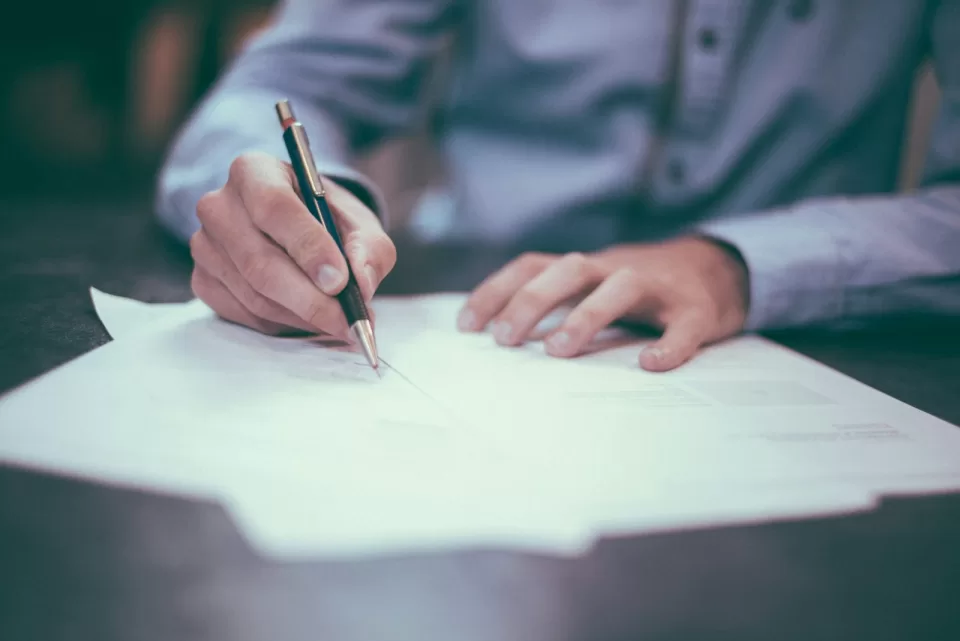 Person signing a printed document with a pen