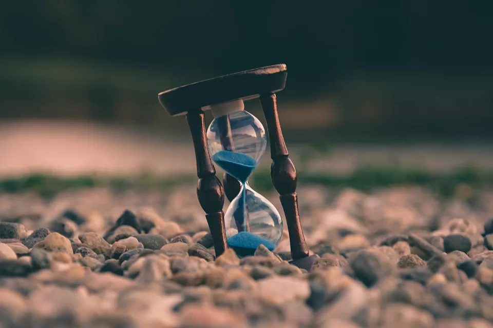 Hourglass with blue sand standing on a pebbled surface