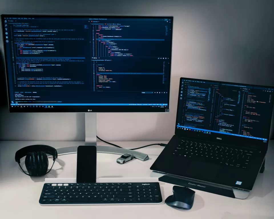 Desk with a monitor and laptop both showing code in a dark editor