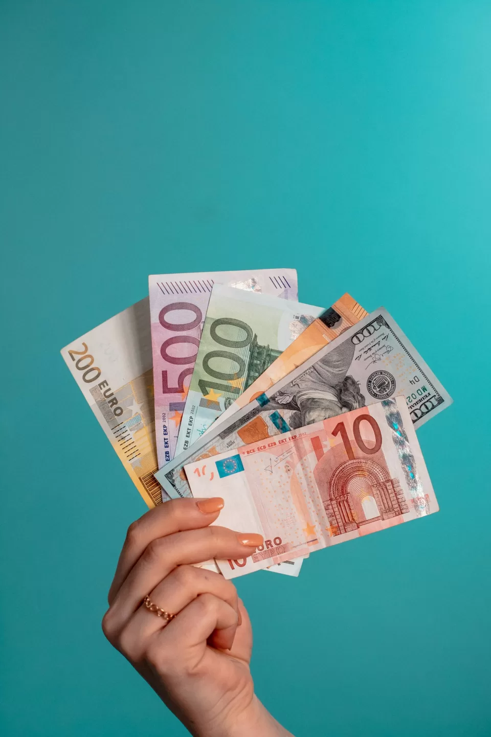 Hand holding a fan of euro and dollar banknotes against a teal background