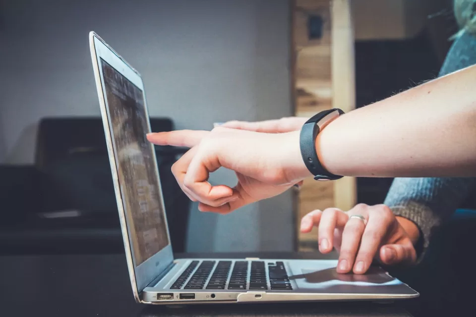 Person pointing at a laptop screen while working at a desk