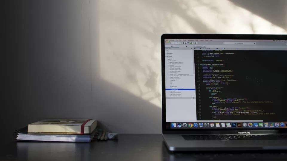 Laptop with code on screen on a desk beside a stack of books