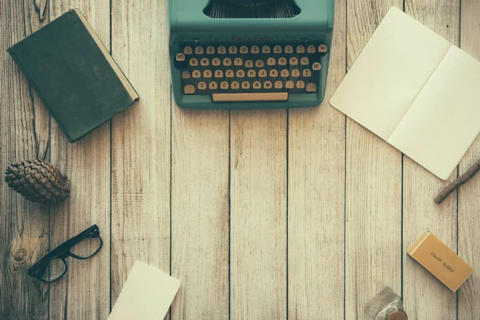 Wooden desk seen from above with a typewriter, notebook and glasses